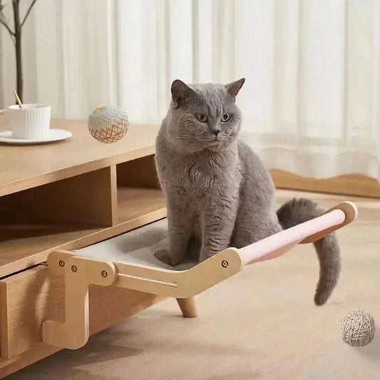 Gray cat sitting on a wooden framed cozy cat hammock attached to a wooden furniture piece in a bright room